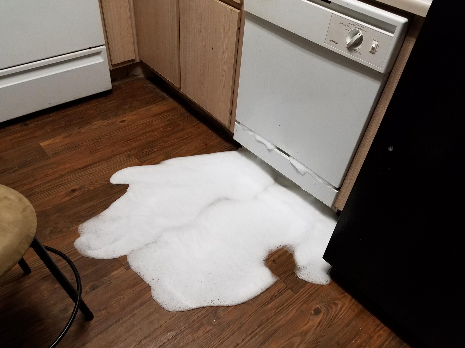 A bottle of dish soap sits next to an empty dishwasher detergent compartment.