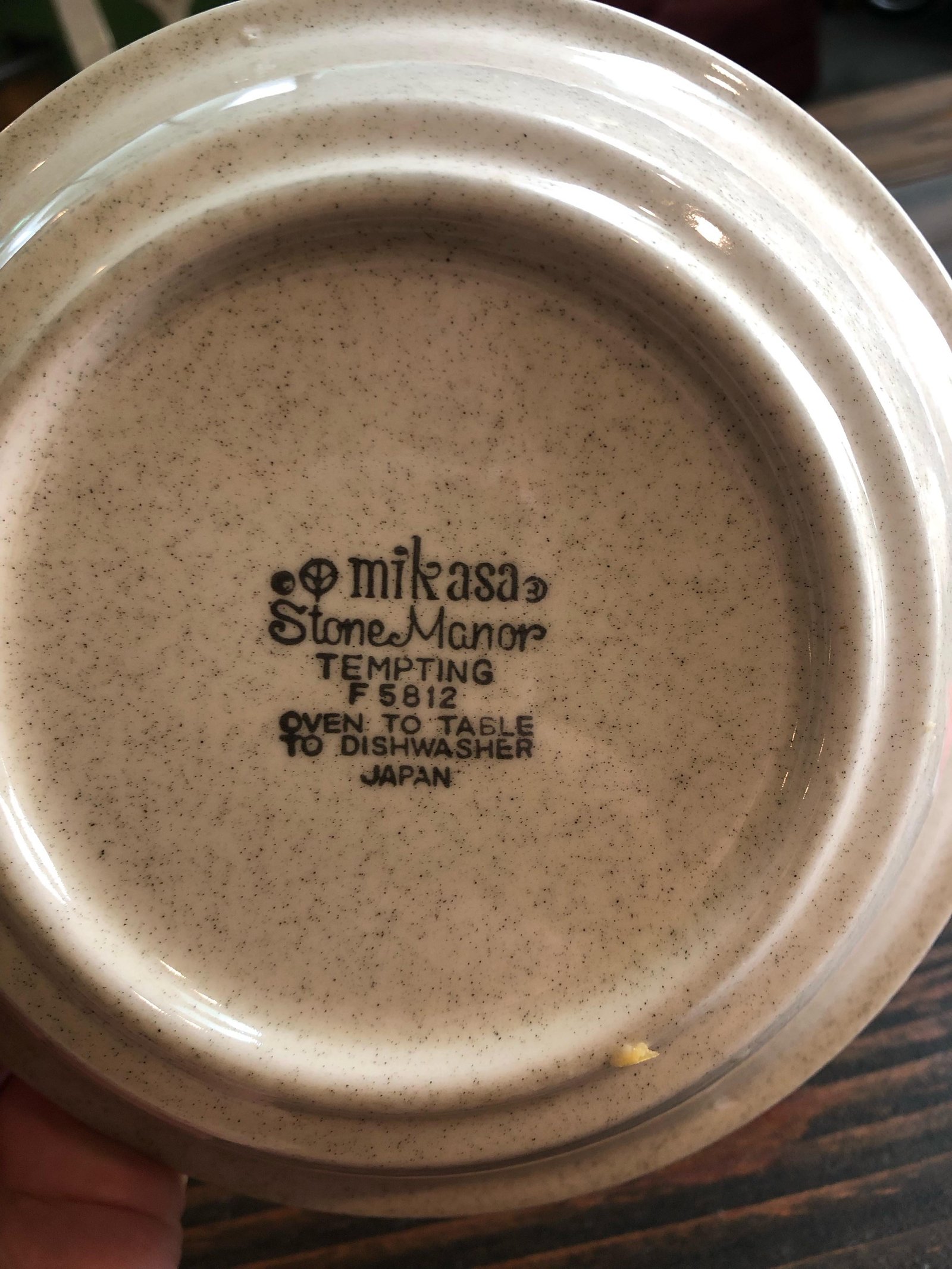 Hands inspecting the maker stamp on the bottom of a stoneware bowl for care instructions.