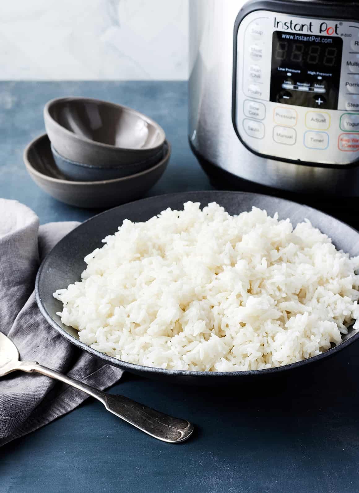 A modern rice cooker sits on a counter next to dry minute rice grains.