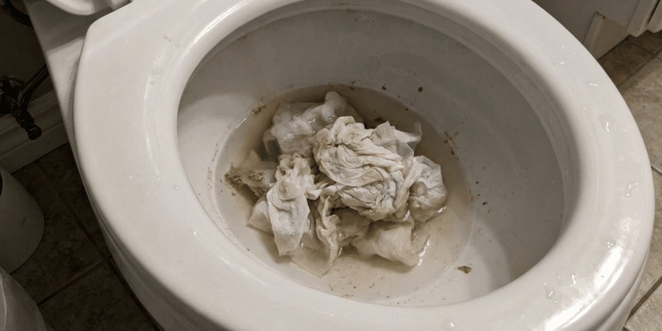 A roll of paper towels placed on a toilet seat showing plumbing hazards.