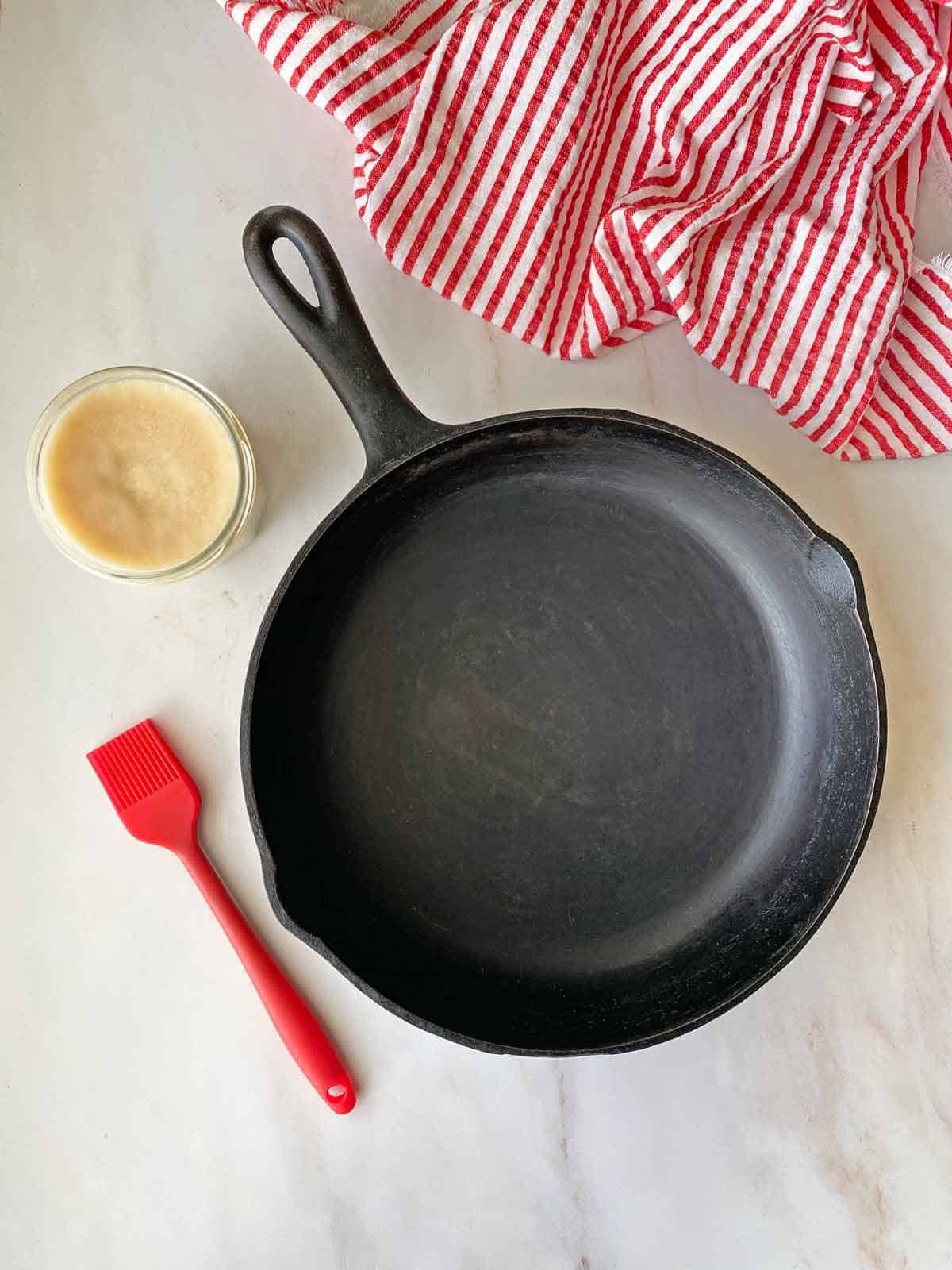 A jar of strained bacon grease sits next to a cast iron skillet.