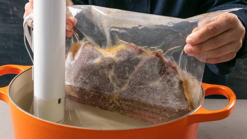 A frozen beef steak ready for sous vide preparation on a wooden surface.