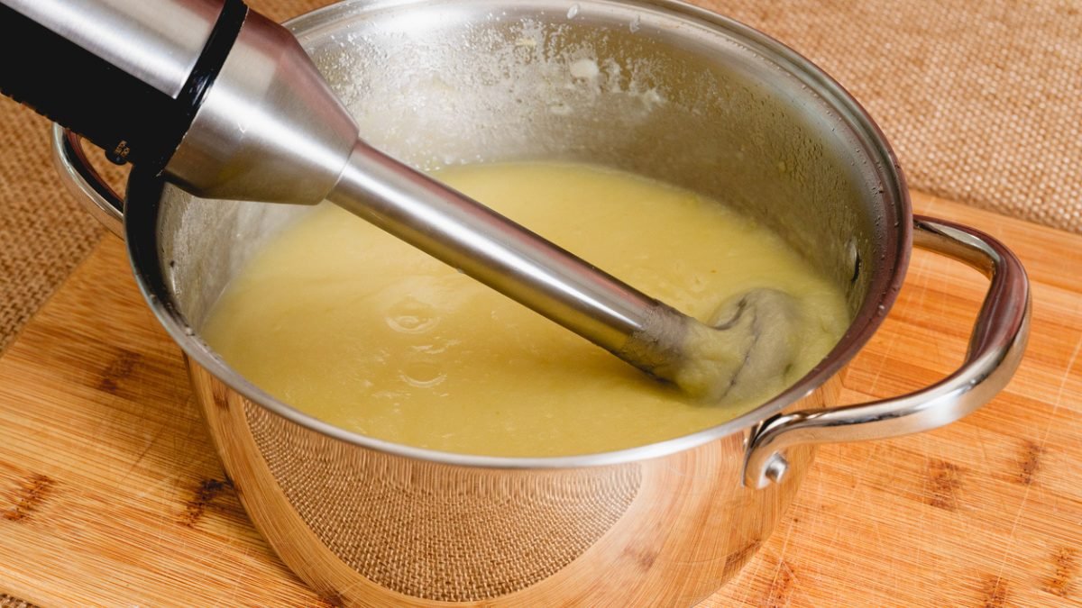 A metal potato ricer creates fluffy strands of potato into a glass bowl.